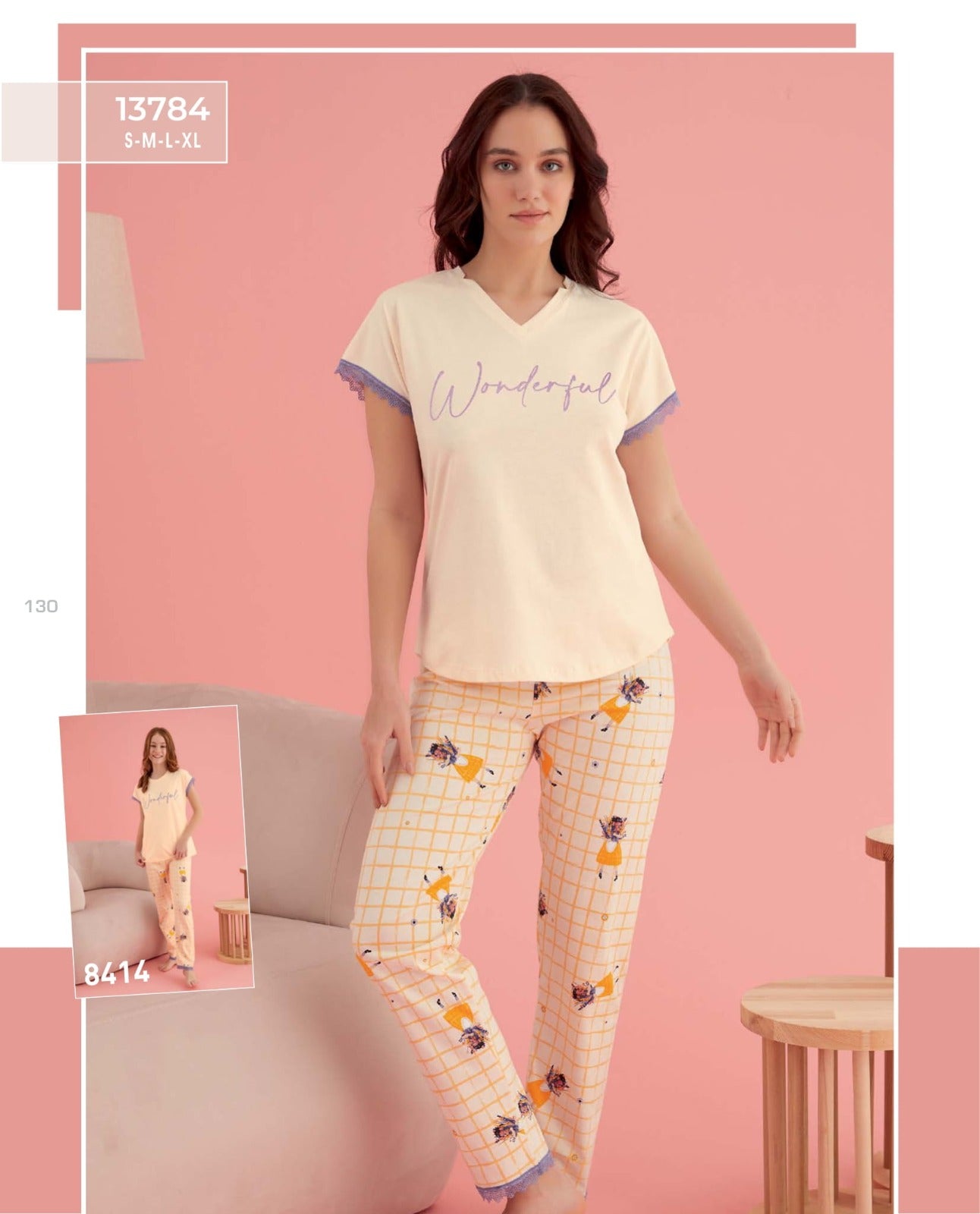Model wearing the Wonderful Pyjama Set by Popjammies, featuring a cream top with lace trim and the word 'Wonderful' in script, paired with yellow grid patterned pants with floral illustrations, standing in a pink-themed room.