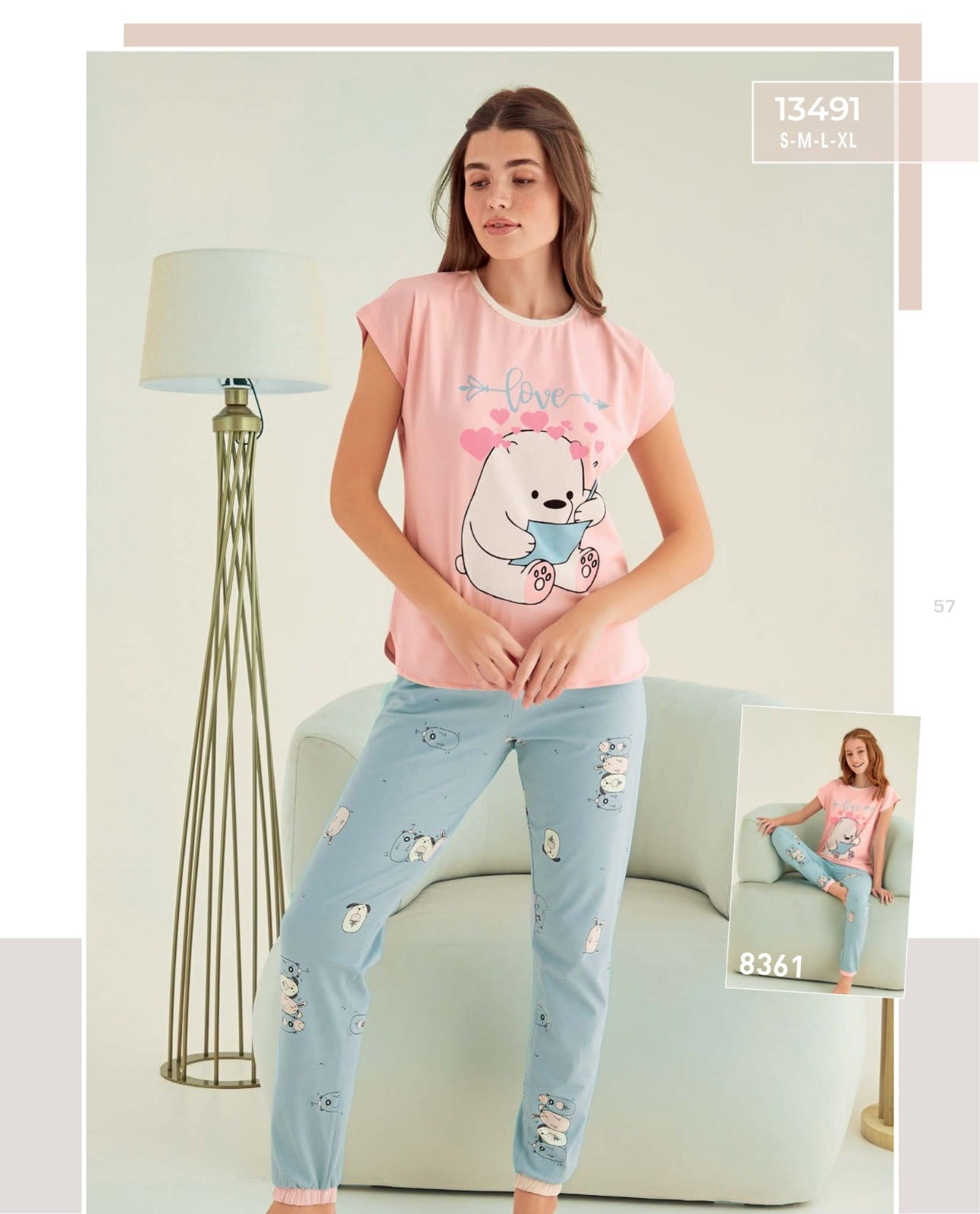Model wearing the Love Bear Pyjama Set by Popjammies, featuring a pink top with a bear and heart design and matching blue pants with bear prints, standing next to a lamp.