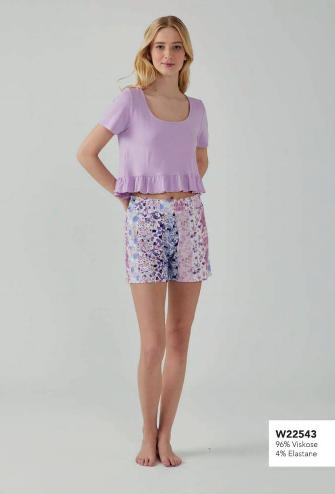 Woman wearing Popjammies Lilac Ruffle Hem Pyjama Set with a lilac top and pastel floral print shorts.