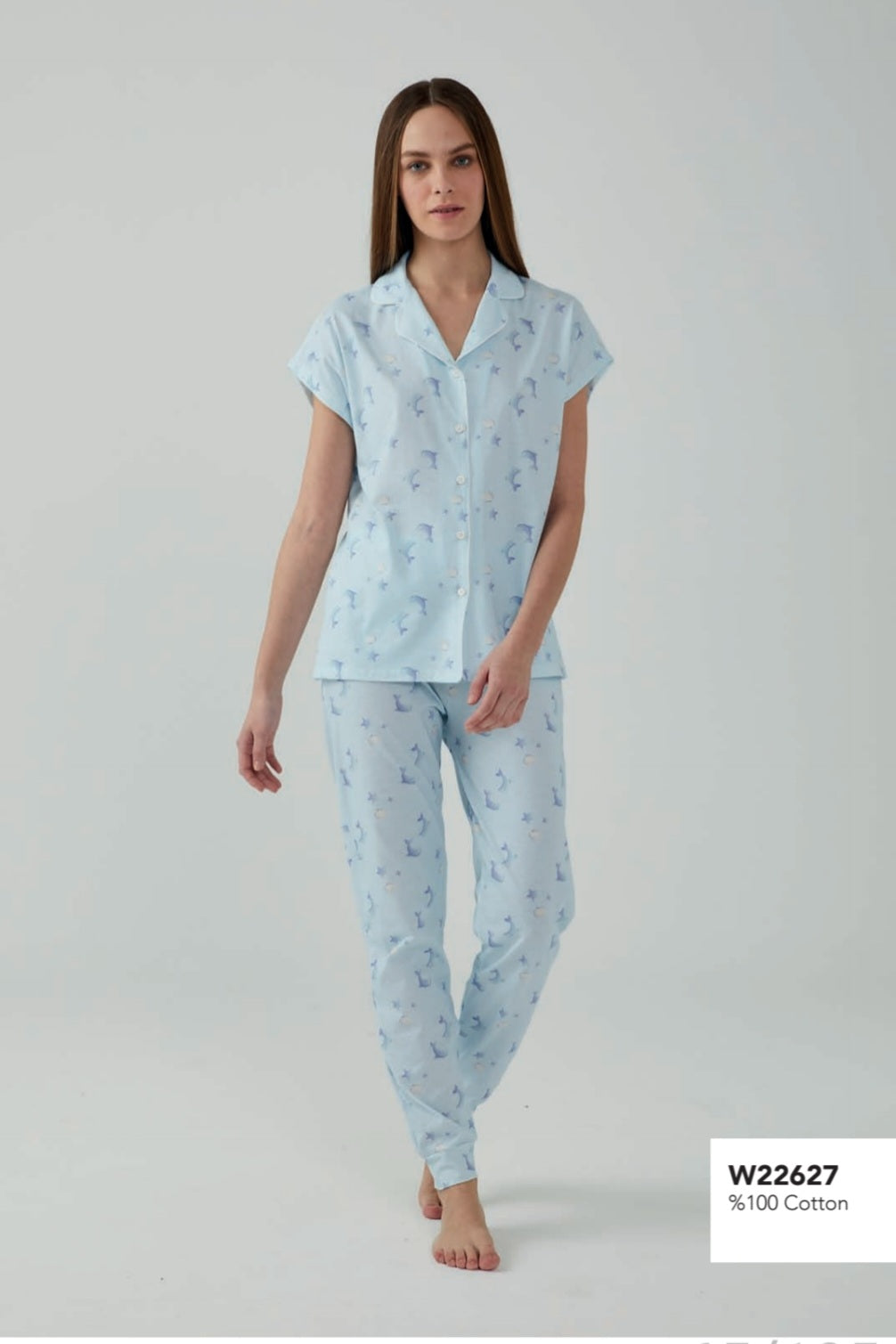 Model wearing a Popjammies blue dolphin print pyjama set, featuring a short-sleeve button-down top and matching pants, walking barefoot.