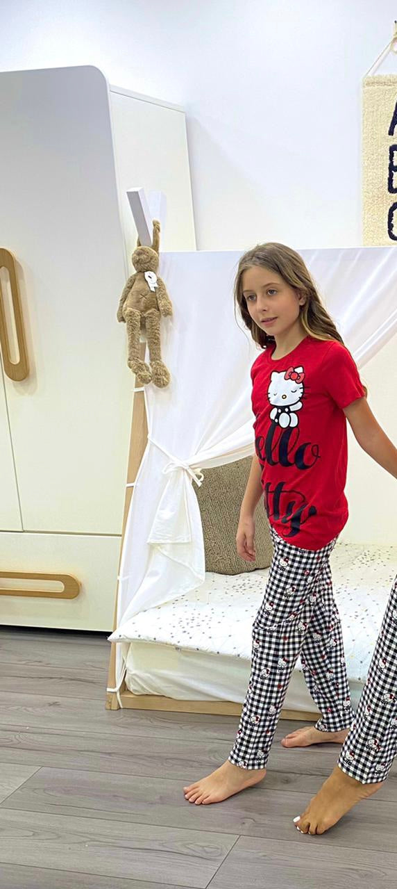 Child wearing Hello Kitty Red and Black Checkered Kids Pyjama Set from Popjammies, featuring a red top with Hello Kitty graphic and black and white checkered pants standing in a room.